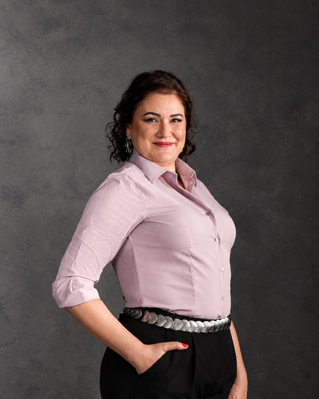 Retrato de Fernanda Carrozza, de camisa rosa, sorrindo com a mão no bolso